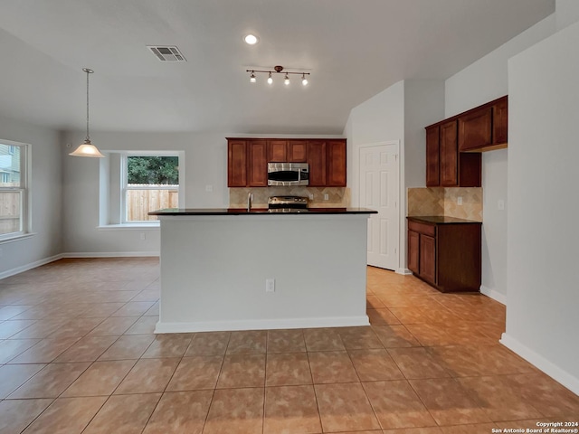 kitchen with backsplash, a kitchen island with sink, light tile patterned floors, and appliances with stainless steel finishes