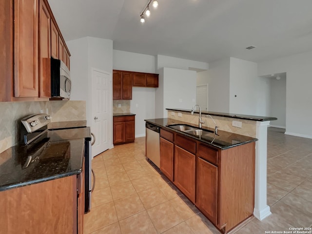 kitchen featuring sink, tasteful backsplash, dark stone counters, a kitchen island with sink, and appliances with stainless steel finishes