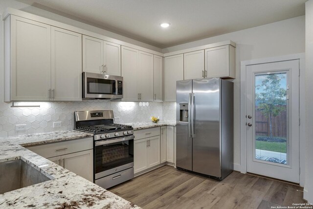 kitchen featuring appliances with stainless steel finishes, backsplash, white cabinets, light stone countertops, and light wood-type flooring