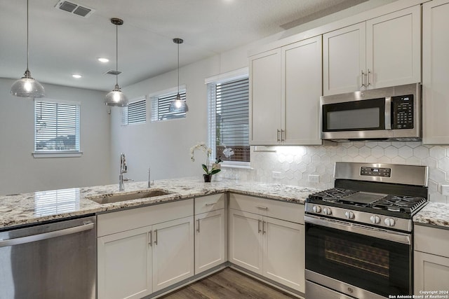 kitchen with appliances with stainless steel finishes, sink, white cabinets, hanging light fixtures, and light stone counters