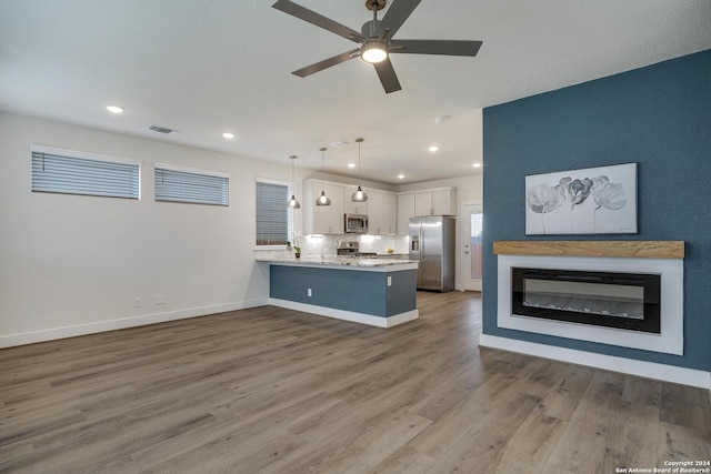 kitchen featuring appliances with stainless steel finishes, wood-type flooring, white cabinets, decorative light fixtures, and kitchen peninsula