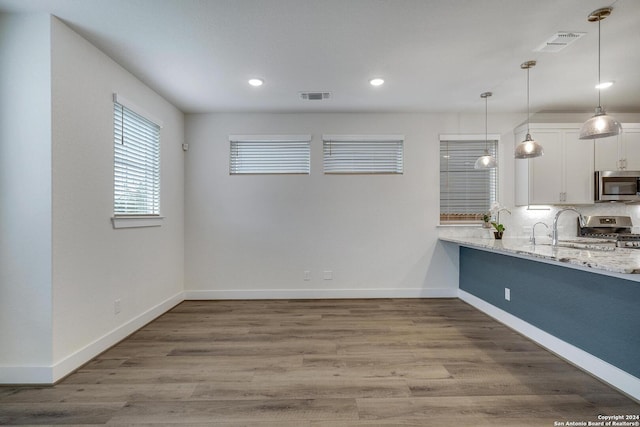 kitchen featuring wood-type flooring, hanging light fixtures, appliances with stainless steel finishes, light stone countertops, and white cabinets