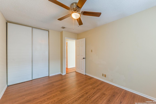 unfurnished bedroom featuring ceiling fan, a closet, a textured ceiling, and hardwood / wood-style flooring