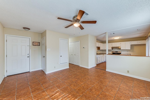 unfurnished living room featuring a textured ceiling, dark tile patterned floors, and ceiling fan