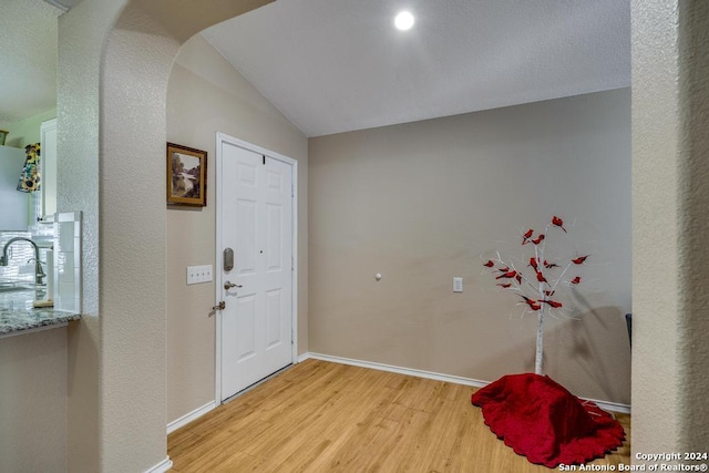 foyer with light wood-type flooring, sink, and vaulted ceiling