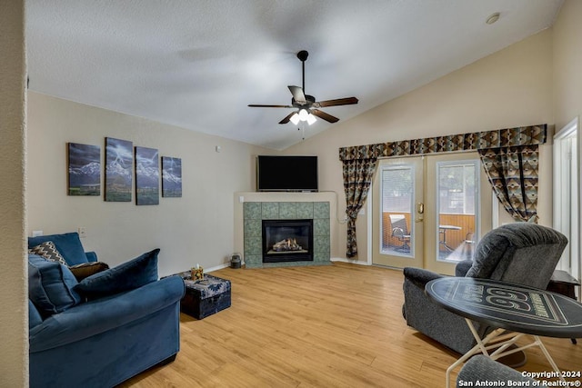 living room with wood-type flooring, vaulted ceiling, ceiling fan, and a tiled fireplace