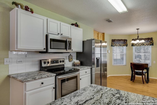 kitchen featuring white cabinets, decorative backsplash, light stone countertops, appliances with stainless steel finishes, and wood-type flooring