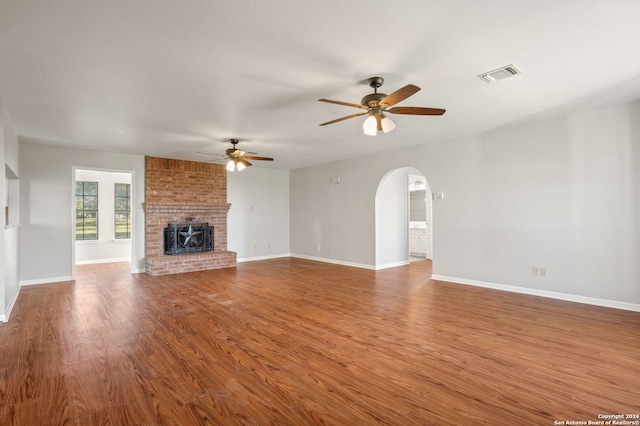 unfurnished living room with hardwood / wood-style flooring, a brick fireplace, and ceiling fan