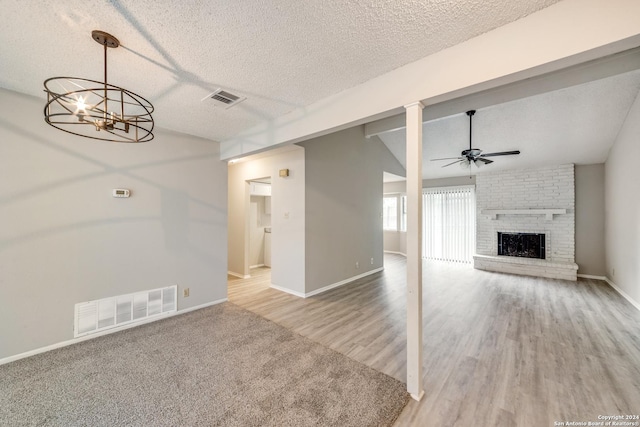 unfurnished living room featuring hardwood / wood-style floors, vaulted ceiling, a textured ceiling, a fireplace, and ceiling fan with notable chandelier