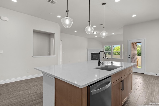 kitchen with sink, dishwasher, hardwood / wood-style floors, hanging light fixtures, and an island with sink