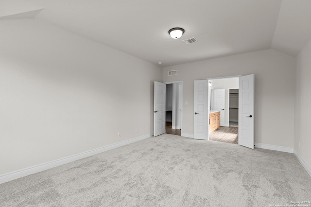 unfurnished bedroom featuring carpet floors, lofted ceiling, and connected bathroom