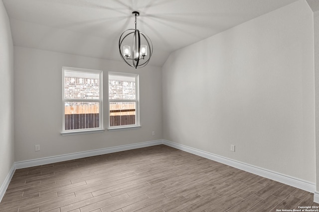 empty room with lofted ceiling, light hardwood / wood-style floors, and a notable chandelier