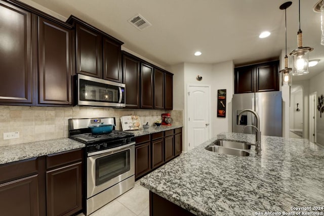 kitchen featuring appliances with stainless steel finishes, light stone counters, sink, light tile patterned floors, and hanging light fixtures