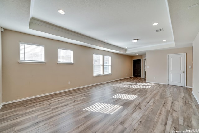 spare room featuring a tray ceiling, light hardwood / wood-style floors, and a textured ceiling