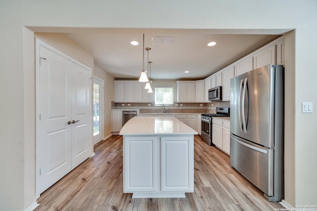 kitchen featuring sink, light hardwood / wood-style flooring, appliances with stainless steel finishes, decorative light fixtures, and a kitchen island