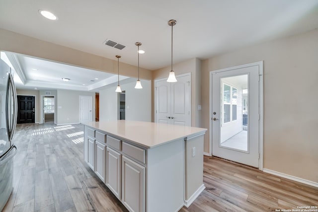 kitchen featuring stainless steel refrigerator, white cabinetry, a center island, hanging light fixtures, and light hardwood / wood-style flooring