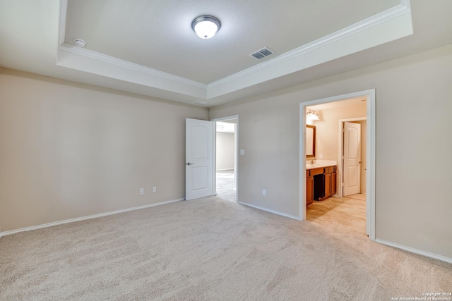 unfurnished bedroom with ensuite bathroom, a raised ceiling, light colored carpet, and crown molding