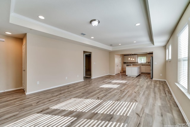 unfurnished living room featuring a healthy amount of sunlight, a raised ceiling, and ornamental molding