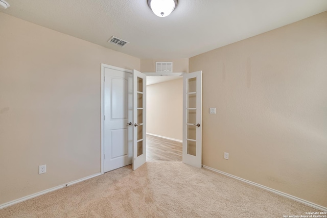 spare room featuring light colored carpet and french doors