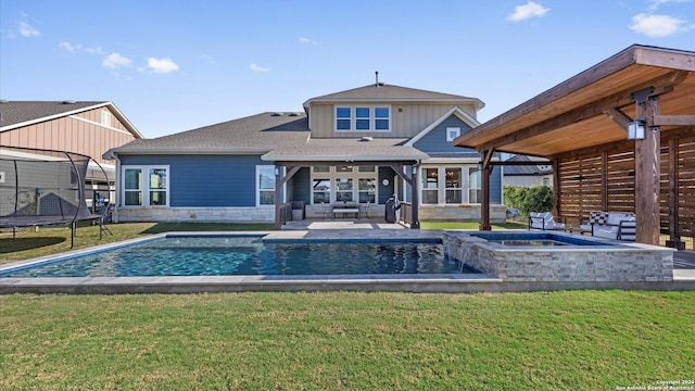 rear view of house featuring an outdoor hangout area, a swimming pool with hot tub, a patio area, a yard, and a trampoline