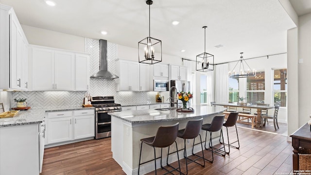 kitchen featuring white cabinetry, stainless steel appliances, wall chimney range hood, dark hardwood / wood-style floors, and a kitchen island with sink