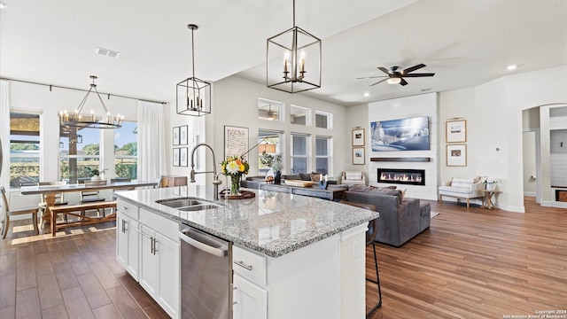 kitchen with white cabinets, sink, an island with sink, a large fireplace, and light stone counters