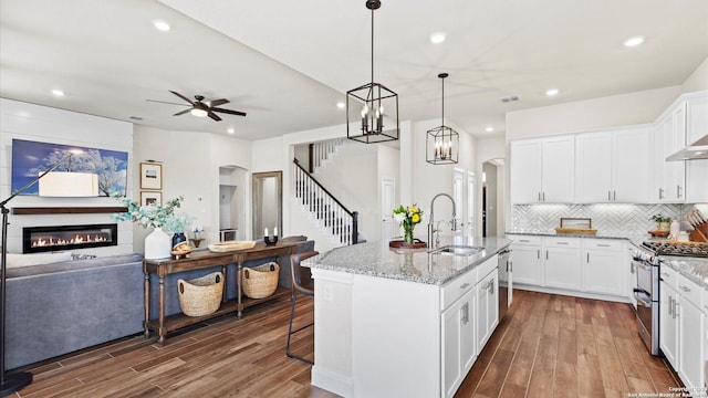 kitchen with white cabinetry, sink, stainless steel appliances, wood-type flooring, and a center island with sink