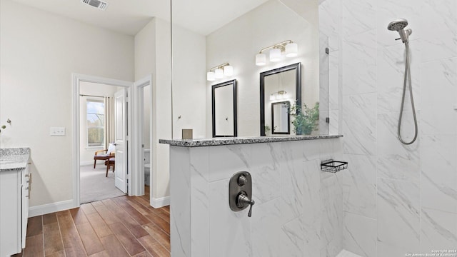 bathroom with a tile shower, vanity, wood-type flooring, and toilet