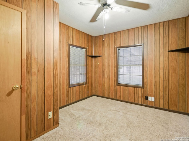 spare room featuring ceiling fan, wooden walls, carpet, and a textured ceiling