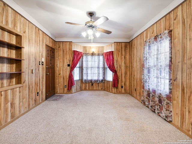 carpeted spare room with ceiling fan, wood walls, and crown molding