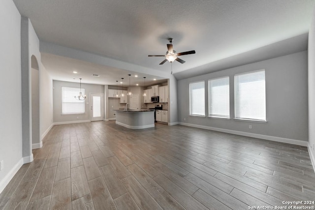 unfurnished living room with ceiling fan with notable chandelier, light wood-type flooring, and sink