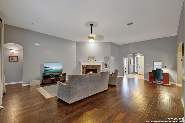 living room with a brick fireplace, ceiling fan, and dark wood-type flooring