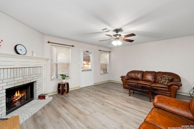 living room featuring a brick fireplace, light hardwood / wood-style flooring, and ceiling fan