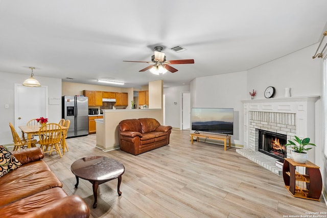 living room featuring ceiling fan, light wood-type flooring, and a brick fireplace