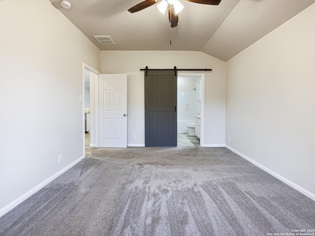 unfurnished bedroom with light carpet, ceiling fan, a barn door, connected bathroom, and lofted ceiling