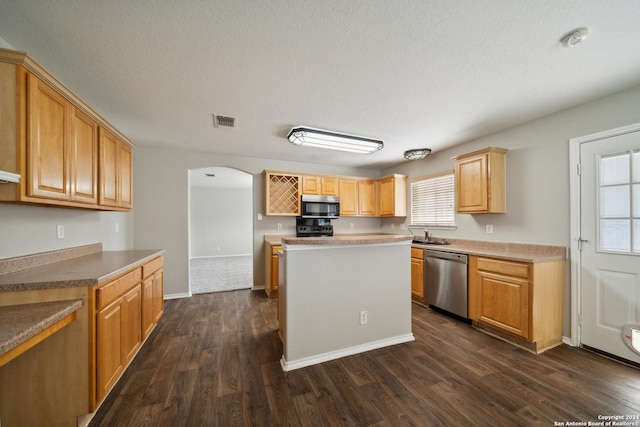 kitchen with a center island, light brown cabinets, dark wood-type flooring, stainless steel appliances, and a textured ceiling