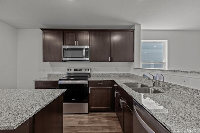 kitchen featuring light stone countertops, dark brown cabinetry, stainless steel appliances, dark wood-type flooring, and sink