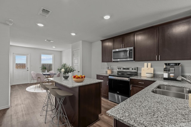 kitchen featuring light stone counters, stainless steel appliances, dark wood-type flooring, sink, and a kitchen island