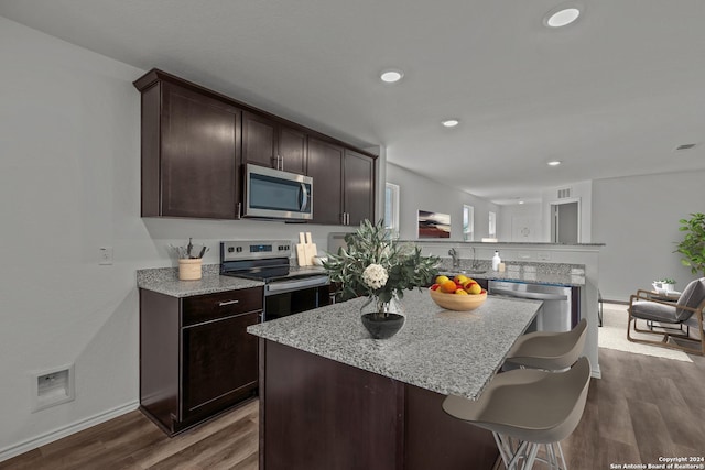 kitchen with a kitchen bar, appliances with stainless steel finishes, dark brown cabinets, and hardwood / wood-style floors