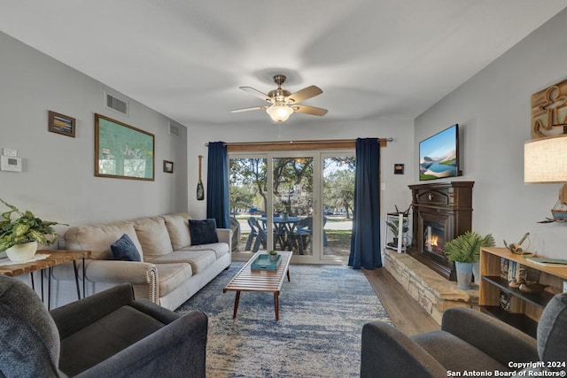 living room with a stone fireplace, ceiling fan, and light wood-type flooring