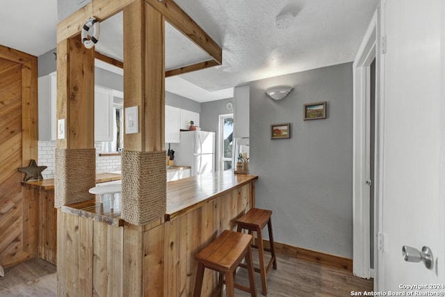 kitchen with white refrigerator, white cabinetry, backsplash, and light hardwood / wood-style flooring