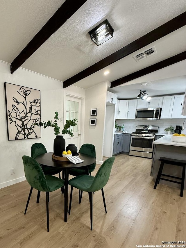 dining area featuring beam ceiling, light hardwood / wood-style floors, and a textured ceiling