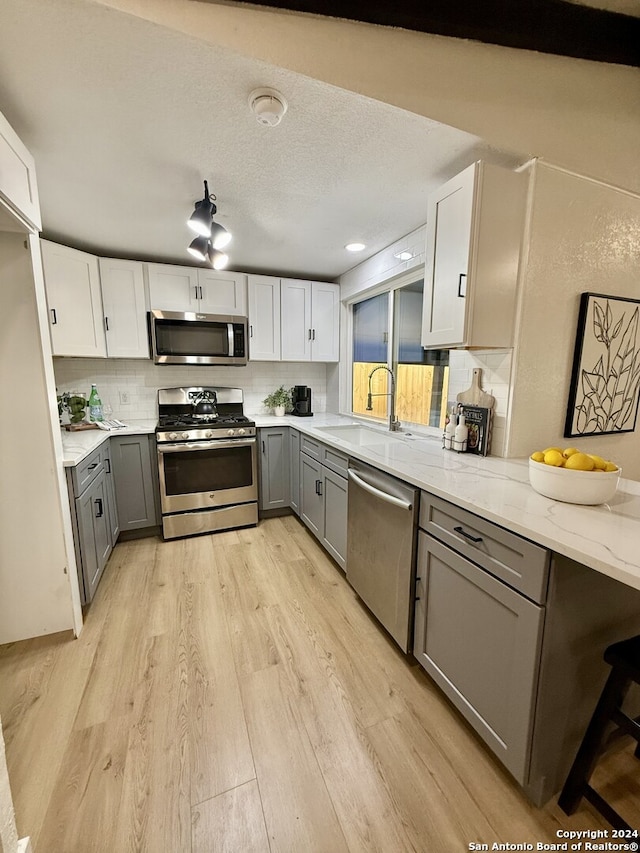 kitchen with light hardwood / wood-style flooring, backsplash, gray cabinets, white cabinets, and appliances with stainless steel finishes