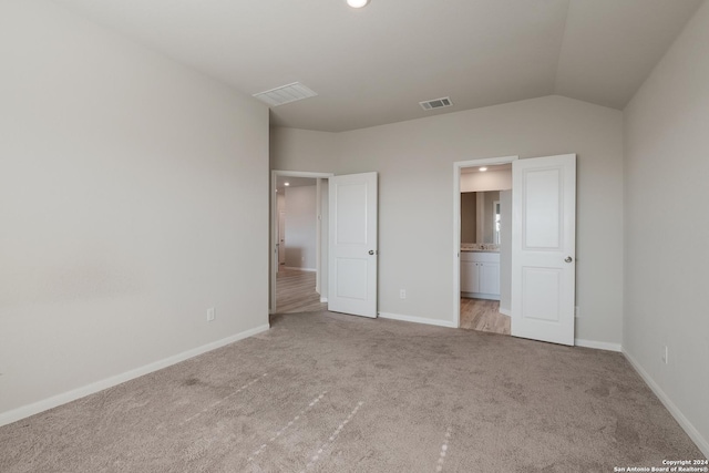 unfurnished bedroom featuring connected bathroom, light colored carpet, and lofted ceiling