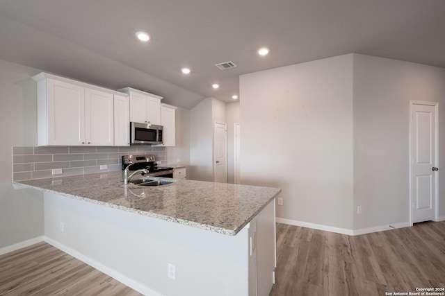 kitchen featuring kitchen peninsula, appliances with stainless steel finishes, decorative backsplash, light stone countertops, and white cabinetry