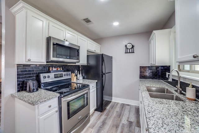 kitchen with white cabinets, sink, light hardwood / wood-style flooring, decorative backsplash, and appliances with stainless steel finishes