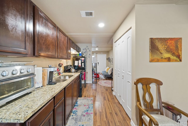 kitchen with light stone counters, sink, light hardwood / wood-style floors, and dark brown cabinets