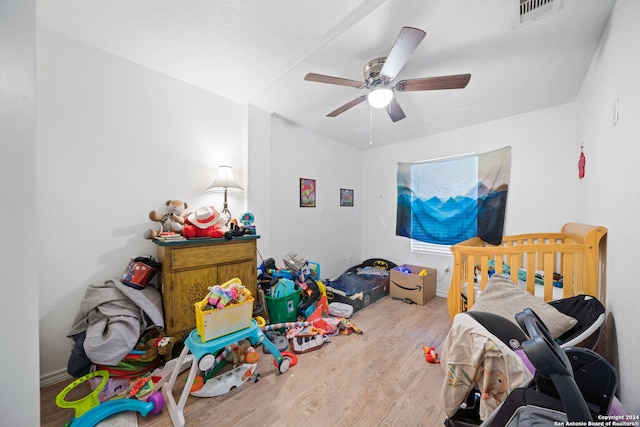 bedroom with wood-type flooring, a nursery area, and ceiling fan