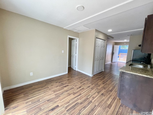 kitchen with hardwood / wood-style floors, light stone counters, dark brown cabinets, and sink