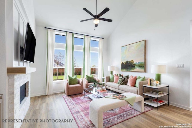 living room with a brick fireplace, ceiling fan, high vaulted ceiling, and light hardwood / wood-style flooring